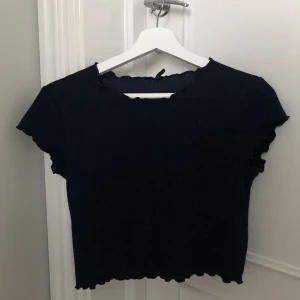Kortärmad topp - Superfin, mörkblå topp med pyttesmå ”vollanger” i ärmarna och nere vid mage/rygg! Den är stretch så passar för både små och större former🥰