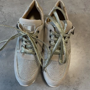 Beiga skor - Beiga skor med guldiga snören samt silvriga detaljer.  Aldrig använt!