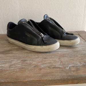 Svarta clean 90 zip Arigato skor. I använt skick. Storlek 43. En liten skada under den högra skon orsakad av en sten. 