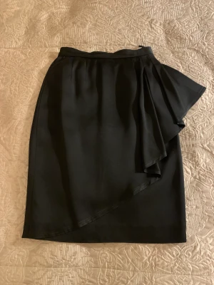 Pennkjol med volang  - Snygg svart pennkjol till knäna finns i storlek 36 med en fin volang på ena höften, säljes för 250 Kr. Jag kan träffas i Stockholm city eller så trycker du på köp knappen så skickar jag den så snabbt jag har packat den bara. 