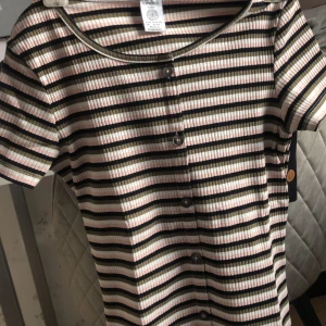 T-shirt  - En fin och färglad t-shirt med knappar på från lindex. Storlek 146/152. Säljer pågrund av att den aldrig kommer till användning