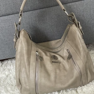 Handväsks - Så fin beige handväska, den är inte lika beige i verkligheten utan lite mer grå. Bild 1 är den korrekta färgen.den har många fack och är väldigt rymlig. Vill du köpa trycker du på ”köp nu” postar alltid samma dag eller dagen efter köp.