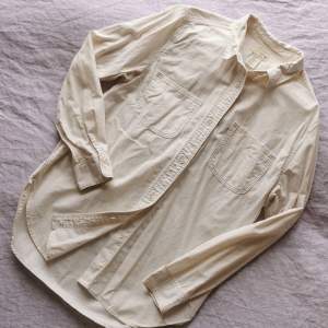 Crèmevit bomullsskjorta med struktur i tyget. Två rundade bröstfickor. Något figorsydd modell. Storlek S. Använd men i bra skick. Axelbredd 40 cm. Längd 72 cm. 