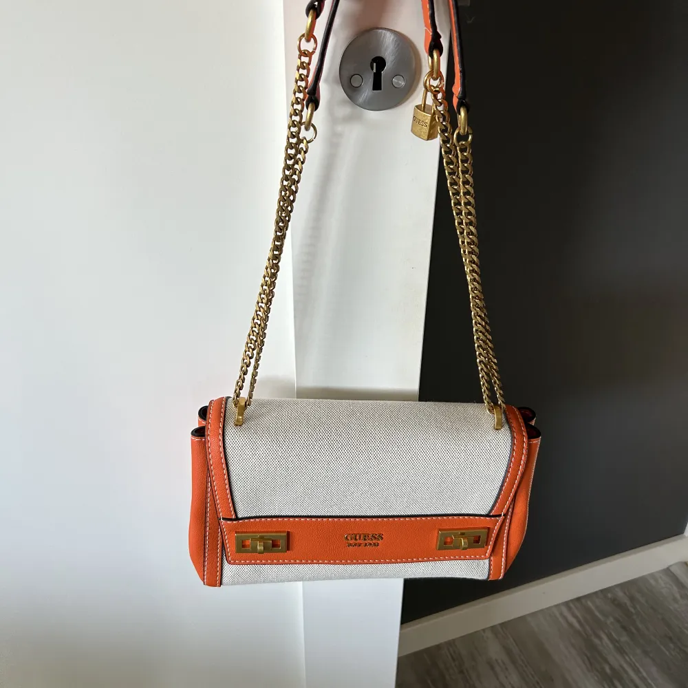 Väska från Guess aldrig använd i orange/beige färg. Längden är 26 vem vidd 8 cm och 16 cm hög. Det går att anpassa Axelsen och använda dem på 2 olika sätt. . Väskor.