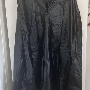 Regnkappa - helt ny - En enkel och praktiskt regnkappa som är enkel att dra över.  Med öppning för armar, ficka på bröstet, dragkedja i halsen och luva  