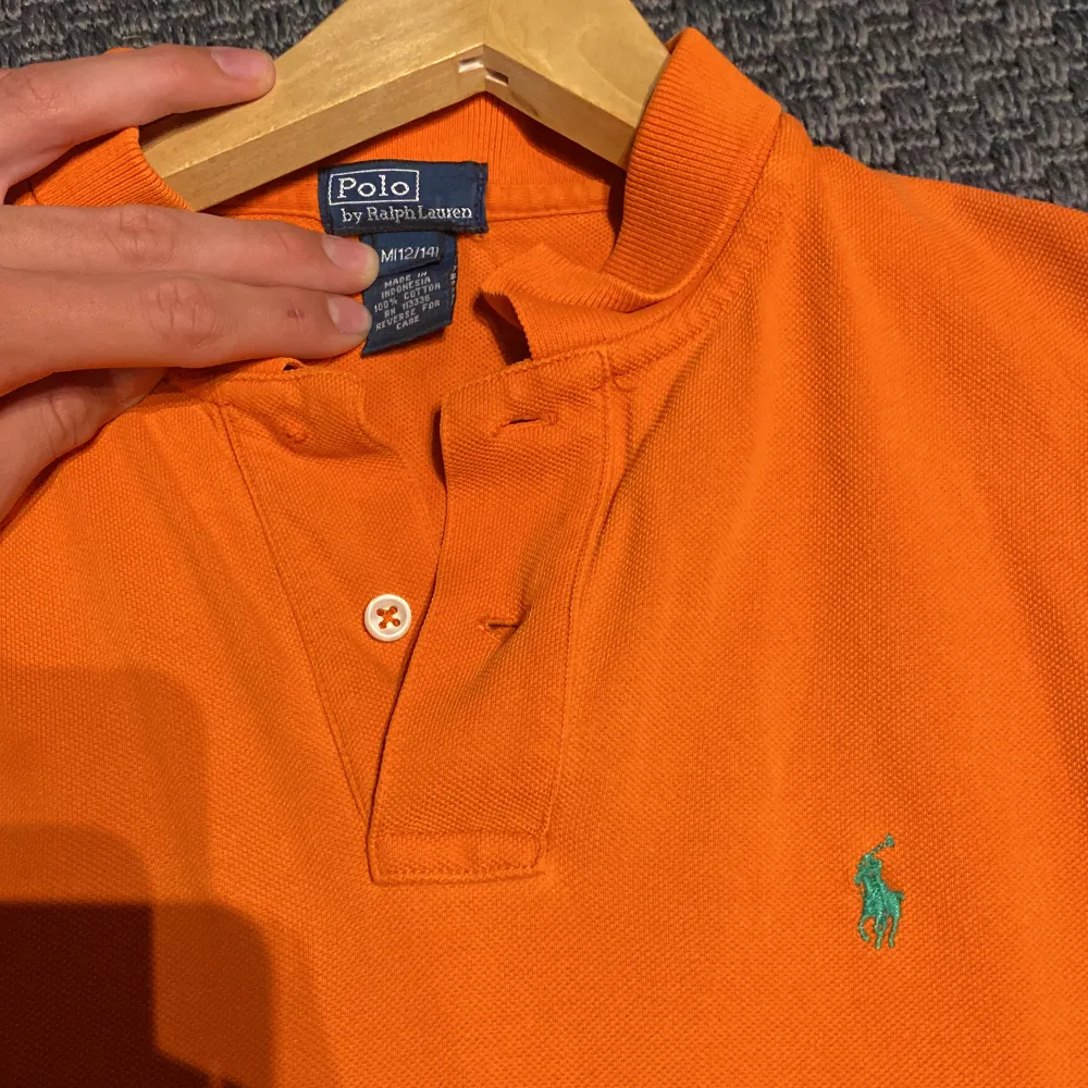 Polo Ralph Lauren tröja i orange. Storleken är medium. En knapp saknas men borde vara enkelt att fixa, sedan litet märke vid nedre delen av tröjan. Det borde ej synas. Skick 7/10. Diskuterbart pris. . T-shirts.