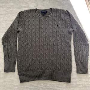 En grå kabelstickad tröja från Ralph Lauren i nyskick. I barnstorleken: L(14-16Y) motsvarar kanske XS.