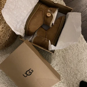 Ugg mini bailey button storlek 38 - Äkta uggs, modell mini bailey button Använda en gång. Originalkartong medföljer Storlek 38 Nypris 2195kr