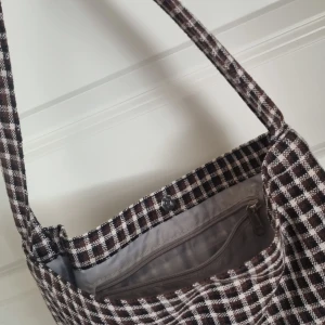 Brunvit väska  - En lite väska i brunt och vitt rut mönster. Väldigt rymlig trots storleck med litet fack inuti. Bra skick, måttligt använd.  Kan diskutera pris. :) 