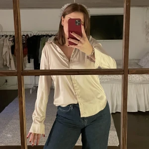 Satin skjorta - Beige skjorta av satin imitation (polyester). Väldigt fin både till vardag och fest! Skicket är bra. Nypris ca 200kr.