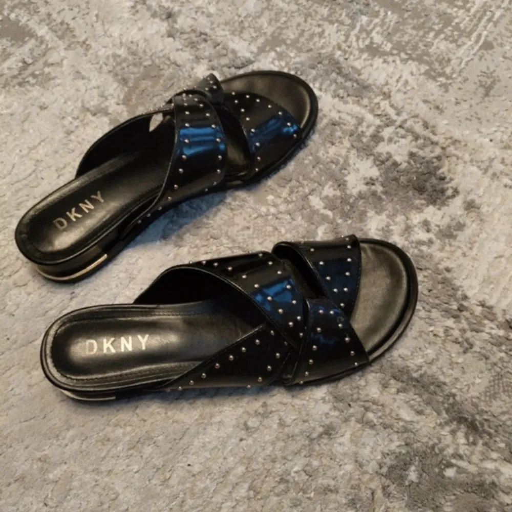 Snygga och bekväma DKNY sandaler i ny skick. Svart läder liknande material med guldiga nitar. Storlek 39. Skor.
