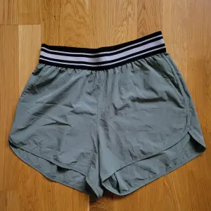 Korta och tunna shorts i en grön/grå färg, de är grönare i verkligheten. Resår i midjan och två fickor. 