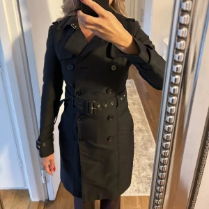 Trenchcoat - Fin trenchcoat. Utanpå är den i väldigt fint skick, dock har innertyget gått sönder vid tvätt därav det låga priset. Den som är händig kan enkelt laga den. Tyvärr så har den inte kommit till så stor användning för mig och hoppas att den får en ñu ägare.