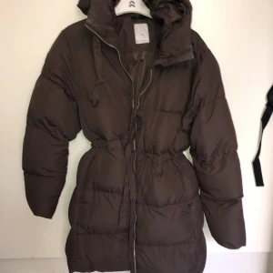 Brun pufferjacket från Etirel - Så snygg o härlig brun pufferjacket från Etirel. Dragsko i midjan och halvlång,går ner över rumpan och en bit till. Färgen är verkligen så fin irl. Luva. Strl 34 men passar men passar även 36.