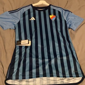 DIF HOME JERSEY 2023 - Säljer denna vackra tröja med radetinac på ryggen! Söker en i storlek M då denna är köpt i fel storlek! Tagg finns kvar (dock avrivet)  Helt oanvänd  Köptes för 1099kr 