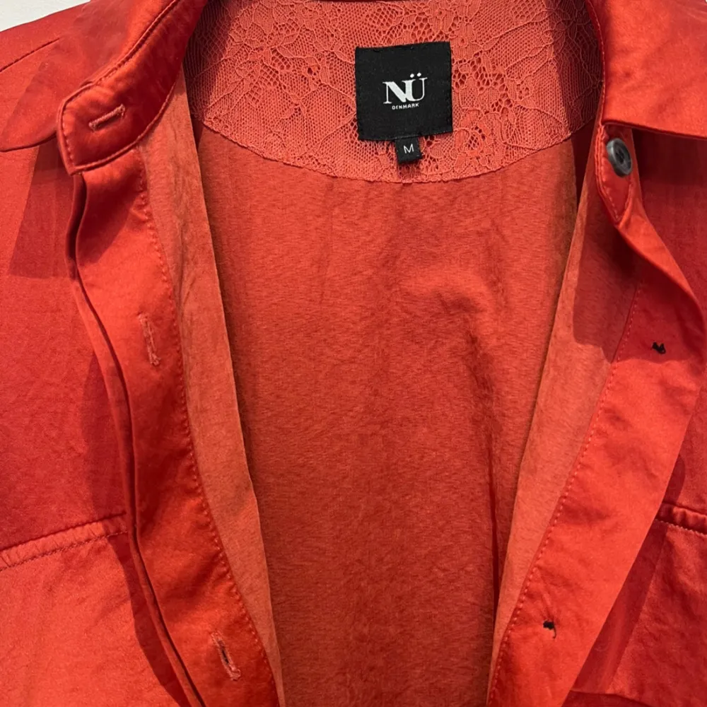 En läcker orangeröd skjortklänning från NÜ Denmark. Skjortklänning kan även användas uppknäppt som en kimono över andra plagg. En riktigt favorit i garderoben som kan användas året om. . Mekot.