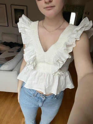 Topp - Vit festtopp med volanger! Från en äldre H&M kollektion så finns inte att köpa längre. Använd ett fåtal gånger så i nyskick! Passar XS-M