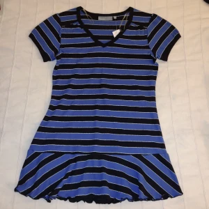 Oanvänd! Randig - blå/svart/silver - y2k kortärmad topp/tunika med volang - Storlek M - Oanvänd y2k randig topp med volang. V-ringad och kortärmad. 50% bomull, 45% polyester och 5% lurex. Mjuk och stretchig. Storlek M (40/42) men passar fler storlekar beroende på hur man vill att den ska sitta. 