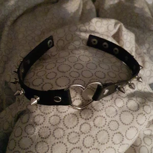 Hjärt choker - En svart tunn choker med ett silver hjärta i mittten. Silver spikarna sitter bra och är inte vassa alls. Man knäpper bara fast chokern hur stor man vill. Har haft i några år men knappast använd. Blivit rengjord specielt. 