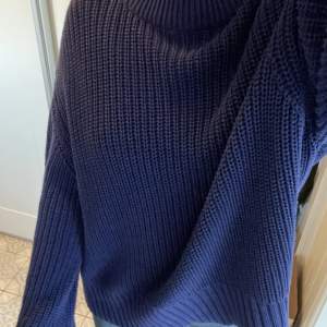 Mörkblå stickad tröja från ginatricot. Tröjan har långa armar som täcker händerna. 