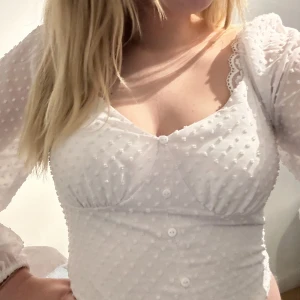 VIT TOPP - Säljer min fina vita somriga topp. Ärmarna är väldigt luftiga och är i ett mycket tunt material, med fina detaljer på. Toppen är figursydd vid bysten, se bild 2. Knapparna går ej att öppna 💕