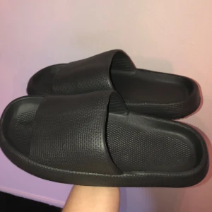 Svarta tofflor i gummi - Dessa svarta tofflor är aldrig använda. De är gjorda av gummi. Som ni ser är kanterna lite ojämna, därav det låga priset. Trots detta är de perfekta för att ha till stranden, som innetofflor eller när du går till tvättstugan.