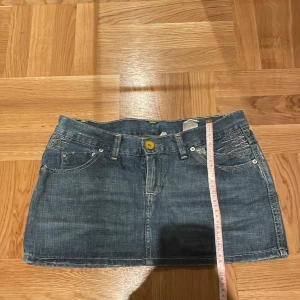 Lågmidjad jeanskjol - En jättefin lågmidjad jeanskjoo med söta detaljer på framtill och på bakfickorna. Jag brukar ha strl 34/xs och denna är stor på mig❤️ Midjemått mätt rakt över: 39cm Längd: 29cm