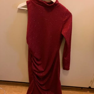 Klänning Boohoo  - En lång och fin klänning som passar till fest. Har fint glitter tyg och har en fin slits på sidan. Har en arm öppen och har en liten halskrage. Är i skönt material, kliar inte. Är helt oanvänd, storlek M/40. 