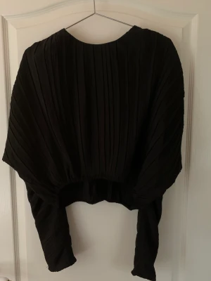 Blus - Svart lite kortare blus med en runt forma, tyget är räfflat