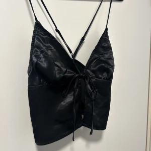 Topp - Linne från H&M i silke/glansigt material. Snöre med knytning mellan brösten, o justerbara axelband som korsar sig i ryggen. Aldrig använd