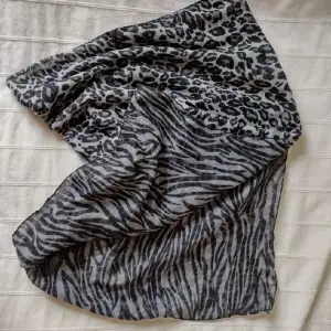 Lång grå/svart djurmönstrad sjal. Olika mönster på fram- och baksida. Nästan 2 m lång och 70 cm bred. En del dragna trådar. Tunn och lätt.
