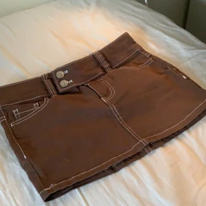 Brun minikjol - Brun jeanskjol med vita detaljer💝 Har kanske använt 1 gång så den är i perfekt skick. Storlek 32/XS