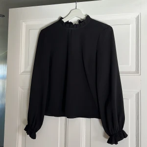 Svart blus  - Knappt använd blus från H&M divided i storlek 34 säljes då jag vuxit ur den. Fina volangdetaljer på ärmarna och runt halsen. Snörning i ryggen. 
