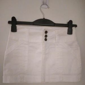 NY, oanvänd vit kort kjol från ONLY. Storlek: 34/XS-SMALL. Helt felfri. - Helt NY och oanvänd kort vit kjol med totalt 4 fickor från ONLY. Har 2 fickor fram och 2 fickor med dragkedja bak, samt hällor för skärp. Storlek: 34/XS. Material: Bomull. Helt felfri/inga defekter. FRAKT TILLKOMMER.