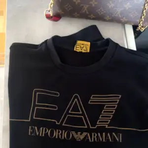 En sällsynt svart Emoprio Armani tröja med guld tryck EA7. I väldigt fint skick! Knappt använd. Storlek S-M Nypris 1800