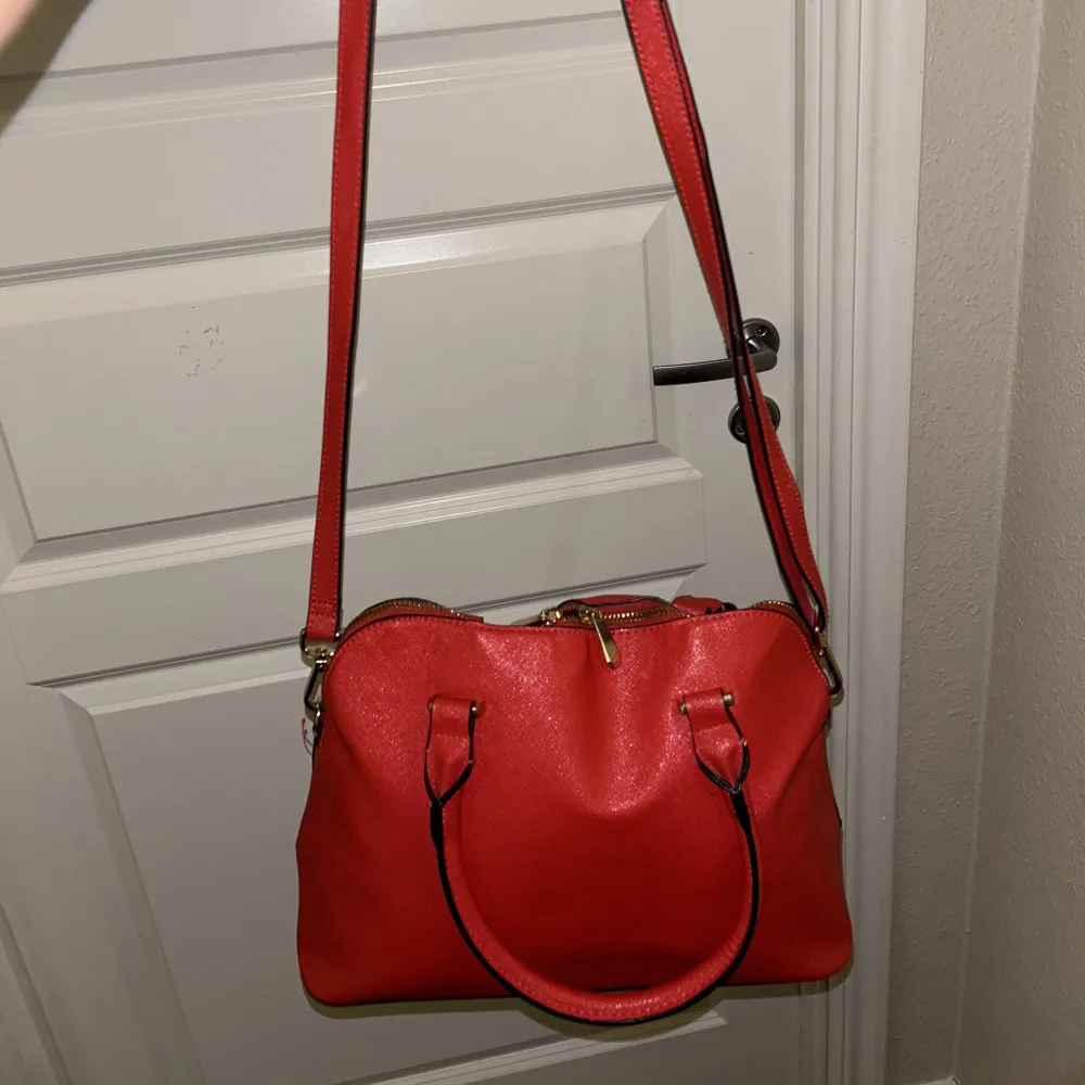 En rosa/röd väska med långt band och kort på varsin sida Jätte fin men används ej . Väskor.