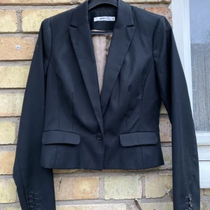 Kavaj, midjekort - Svart kavaj med v-ringning och knapp. Mäter ca 50 cm från axeln till midjan.