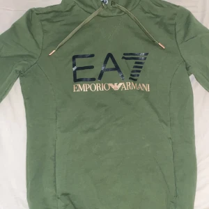 Armani huvtröjor  - Armani huvtröja i olivgrön med gulddetaljer. Fickor framtill. Oanvänd.