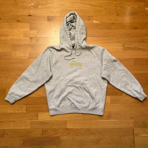 Hoodie från Stüssy med gul text - Jättenajs grå hoodie från Stüssy! Storlek S