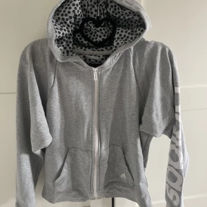 Grå adidas hoodie - Grå hoodie från adidas med dragkedja och logga på ärmen med prickigt mönster i luvan säljes🩶