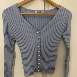 Stickad kofta  - Stickad kofta från NA-KD med pärldetaljer i färgen blå. Koftan är i bra skick. Den säljs fortfarande för 439kr på hemsidan. Jag säljer däremot min för 80kr. Koftan är i storlek S.