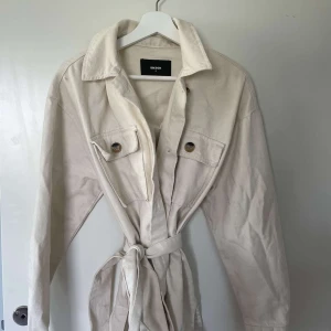 Beige kappa  - Beige kappa med stora fickor, bälte och knappar. Väldigt bra kvalitet, något tjockare. Perfekt jacka för sommarkvällar. Tips! Styla med en snygg hoodie under. 