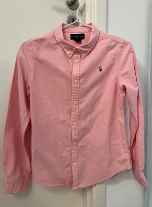 Skjorta Ralp Lauren - Rosa tjejskjorta från Ralph Lauren i fint skick. Storlek 14, men är liten. Jag skulle säga 10-12 år.