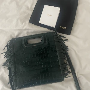Maje väska - Intressekoll på min fina mörkgröna Majeväska. Köpt för ca 6 månader sen i en Majebutik i London för ca 3 900kr. Endast använt några gånger så den är som nyskick, kvitto och dustbag finns.🥰 Pm vid frågor!!