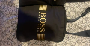Hugo boss väska  - Hej vill sälja min boss väska för att jag har haft den i ett tag blå väska med guldig täxt 