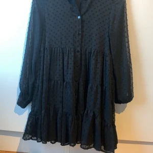Svart klänning - Svart kort klänning med långa ärmar. Har knappar där fram och sitter löst.