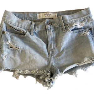 lågmidjade jeansshorts  - ljusblåa lågmidjade abercrombie and fitch jeansshorts med asballa slitningar, skulle säga att dom passar någon med storlek S. Aldrig använda så väldigt bra skick