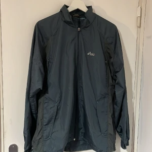 Asics Vindjacka - Asics Vindjacka i snygg blå/grön färg.  Använd ett par gånger men för stor. Utmärkt skick och extremt skön - passar till de flesta vädertyper.