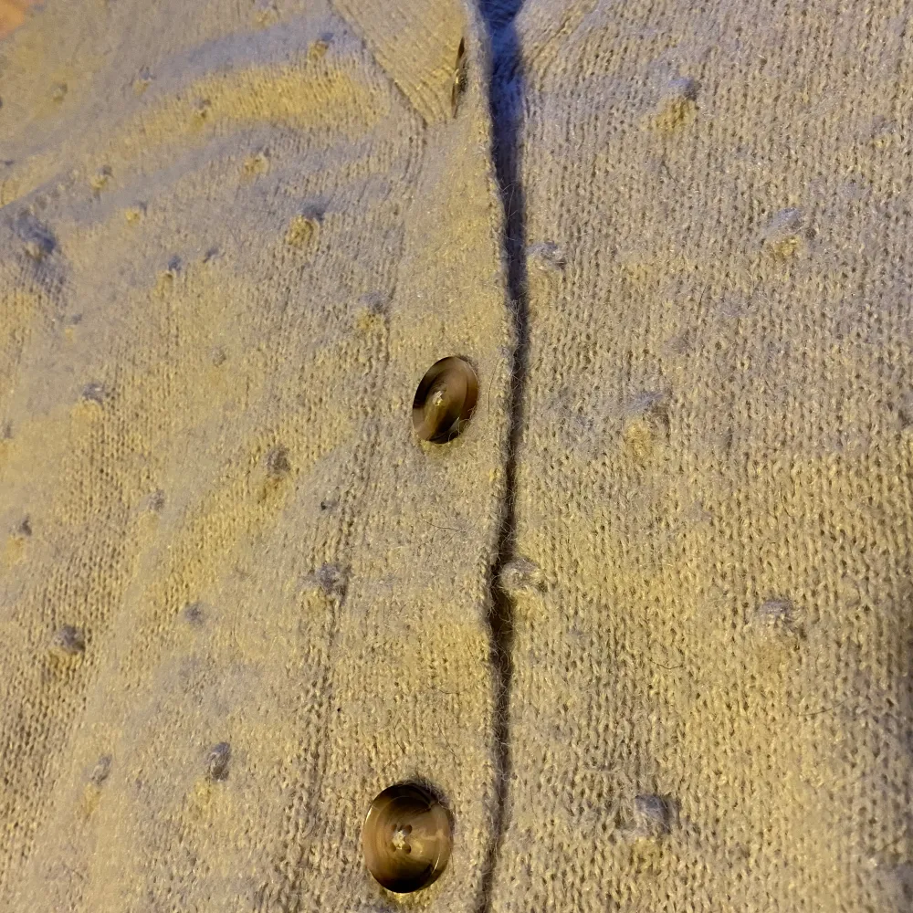 En benvit kofta som man knäpper i fram. Så söt detalj med små ”bollar” som är stickade i tröjan. Så skön i materialet och värmande. Inte så djup i urringningen. . Tröjor & Koftor.