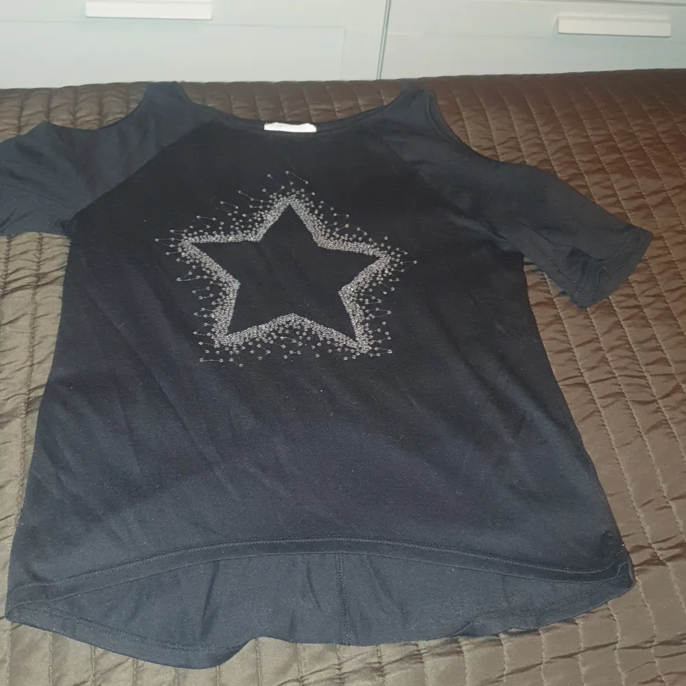 Barn tröja med små paljetter som formar en stjärna. Tröjan är öppen vid armen/ axeln.. T-shirts.